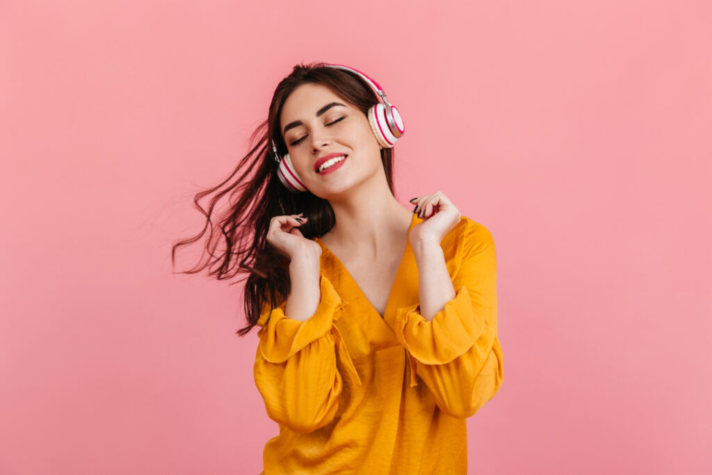 active woman with snow white smile is dancing pink wall model orange blouse listening music